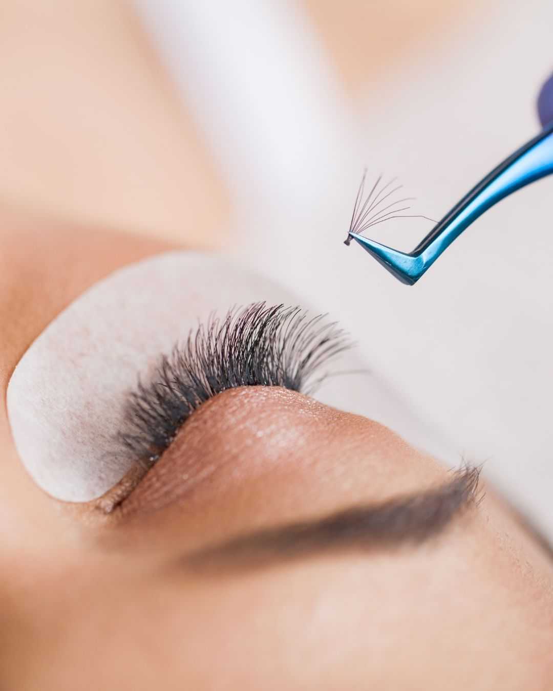 Eyelash extension being carefully applied with tweezers to a closed eye.